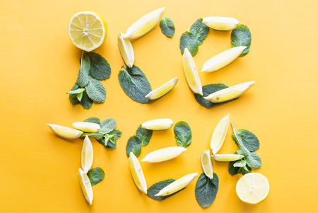 Words cold tea are lined on a bright yellow background from the lobes of lemon and mint. Cold summer drink conceptの写真素材