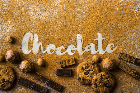 The word chocolate printed on cocoa on a gray background among cocoa and chocolate chip cookies, chocolate pieces, nuts in chocolate and sweets. I love chocolate conceptの写真素材