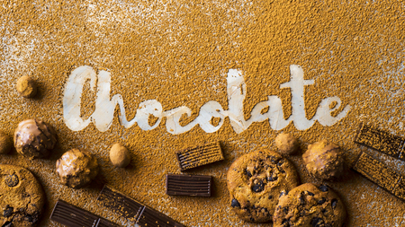 The word chocolate printed on cocoa on a gray background among cocoa and chocolate chip cookies, chocolate pieces, nuts in chocolate and sweets. I love chocolate conceptの写真素材