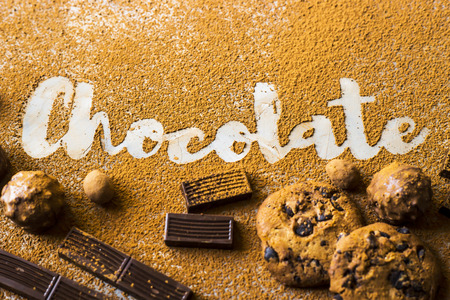 The word chocolate printed on cocoa on a gray background among cocoa and chocolate chip cookies, chocolate pieces, nuts in chocolate and sweets. I love chocolate conceptの写真素材