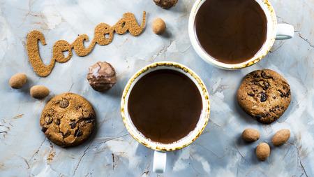 The word cocoa is written in letters of cocoa on a gray concrete background next to two cups of cocoa and chocolate sweets and biscuits. I love the cocoa conceptの写真素材