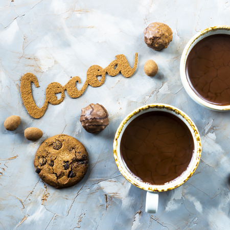 The word cocoa is written in letters of cocoa on a gray concrete background next to two cups of cocoa and chocolate sweets and biscuits. I love the cocoa conceptの写真素材