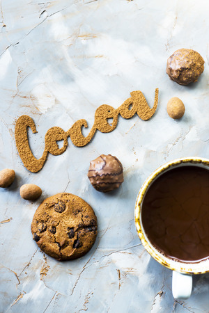 The word cocoa is written in letters of cocoa on a gray concrete background next to two cups of cocoa and chocolate sweets and biscuits. I love the cocoa conceptの写真素材