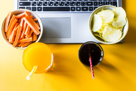 Choose a snack - healthy eating carrots with juice or harmful food chips with cola. Food in the break between working on a laptopの写真素材