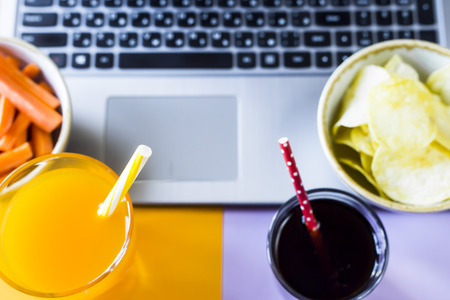 Choose a snack - healthy eating carrots with juice or harmful food chips with cola. Food in the break between working on a laptopの写真素材