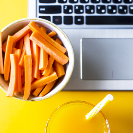 Carrots sliced with straw and a glass of juice, which stands near the laptop. Break from work for a snack. Healthy Food Conceptの写真素材