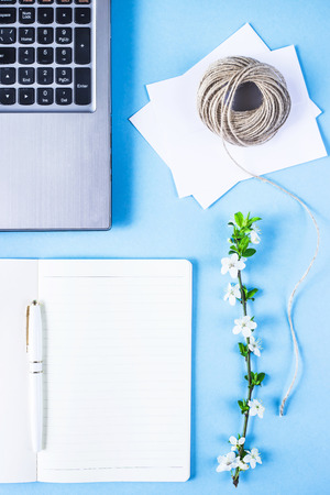 Creative workplace with laptop, notebook, envelopes, twine and flowering branch on a blue background. Spring conceptの写真素材