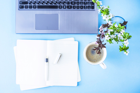 A bouquet of flowering branches on a creative desktop with a laptop and a notebook on a blue backgroundの写真素材