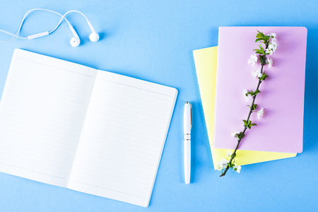 Open notebook with headphones, a cup of tea and colorful notepads on a blue background. Spring workplace with flowering branchesの写真素材