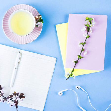 Open notebook with headphones, a cup of tea and colorful notepads on a blue background. Spring workplace with flowering branchesの写真素材