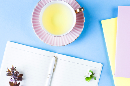 Open notebook with a cup of tea and colored notebooks on a blue background. Spring workplace with flowering branchesの写真素材