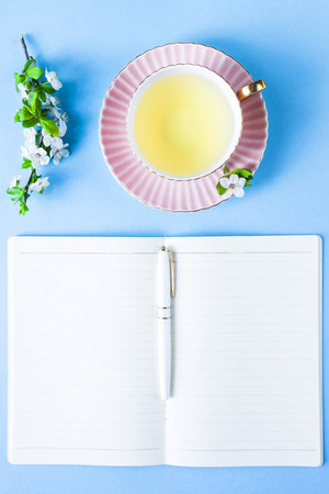 Open notebook with headphones and a cup of tea on a blue background. Spring workplace conceptの写真素材