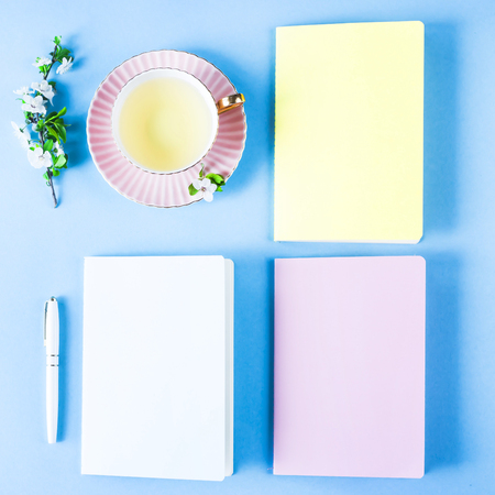Three multicolored notebooks and a cup of tea on a blue background. Spring workplace with flowering branchesの写真素材