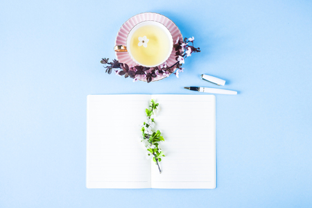 Open notebook next to flowering branches and a cup of tea. Spring workplace conceptの写真素材