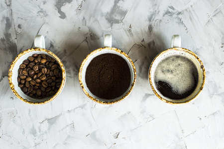Three cups of coffee at different stages of cooking. Ground coffee, coffee beans and ready-made coffee drink. Top view, flat layの写真素材
