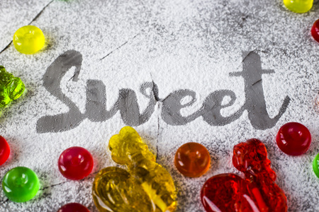 The word sweet is written on a gray concrete background with the help of powdered sugar next to multi-colored sweets and retro candies in the form of cockerels. Top view, flat layの写真素材