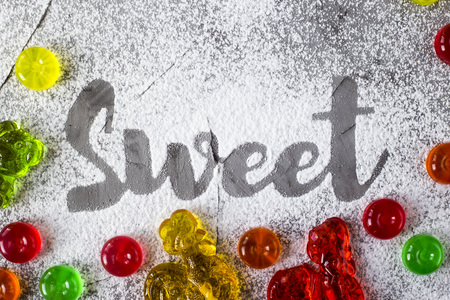 The word sweet is written on a gray concrete background with the help of powdered sugar next to multi-colored sweets and retro candies in the form of cockerels. Top view, flat layの写真素材