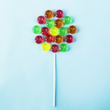 Lollipop on a stick on a blue background of small multi-colored sweets. Top view, flat layの写真素材