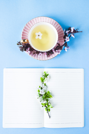Open notebook next to flowering branches and a cup of tea. Spring workplace conceptの写真素材