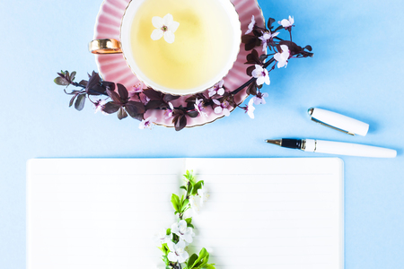 Open notebook next to flowering branches and a cup of tea. Spring workplace conceptの写真素材