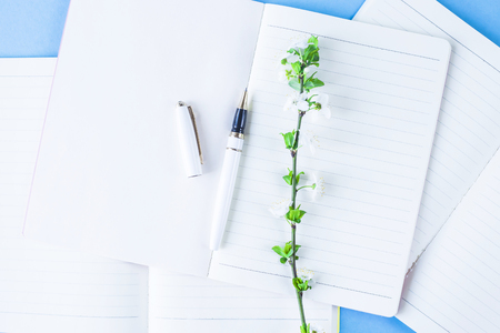 A stack of three notebooks on a creative workplace with flowering branches on a blue background.
Spring workplace concept.の写真素材