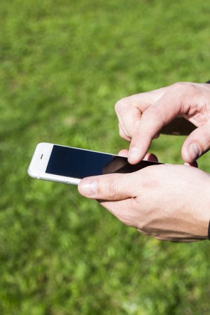 A man uses a smartphone outdoor. Man's hands push on the phone. Modern online lifestyle の写真素材