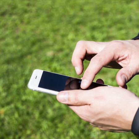 A man uses a smartphone outdoor. Man's hands push on the phone. Modern online lifestyle の写真素材