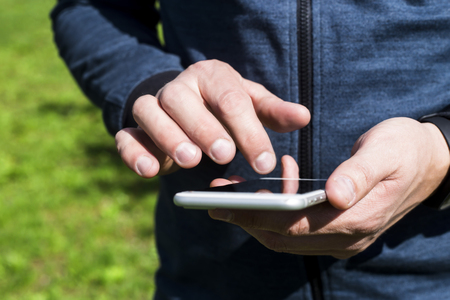 A man uses a smartphone outdoor. Man's hands push on the phone. Modern online lifestyle の写真素材