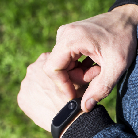 Fitness bracelet or smart watch on a man's hand. Against the background of green grass. An adult male in a blue band. Healthy lifestyle conceptの写真素材