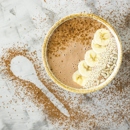 Chocolate-banana smoothies in a bowl on a gray concrete background next to the shape of a spoon of cocoa. Healthy Breakfast Conceptの写真素材