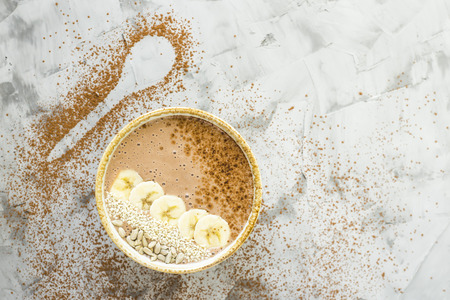 Chocolate-banana smoothies in a bowl on a gray concrete background next to the shape of a spoon of cocoa. Healthy Breakfast Conceptの写真素材