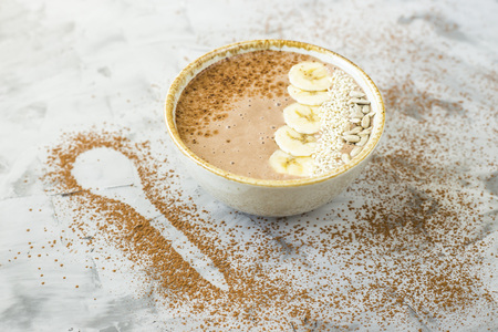 Chocolate-banana smoothies in a bowl on a gray concrete background next to the shape of a spoon of cocoa. Healthy Breakfast Conceptの写真素材