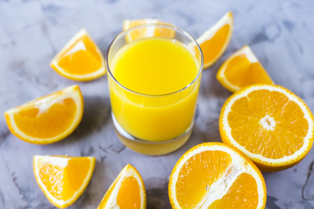 Sliced orange next to a glass of orange juice on a gray backgroundの写真素材