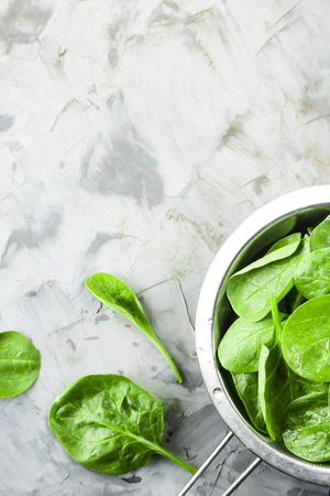 Washed spinach in a metal colander on a gray background. Fresh green leaves for cooking healthy dishesの写真素材