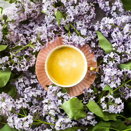 A pink cup of coffee with lilac flowers on a gray concrete table. Spring concept. Top view, flat layの写真素材