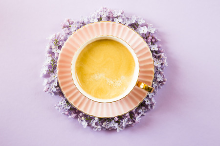 A pink cup of coffee with lilac flowers on a bright purple background. Spring concept. Top view, flat layの写真素材