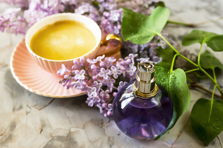 The violet bottle of female perfume stands next to the flowers of lilac and a cup of coffee. Spring fragrance for womenの写真素材