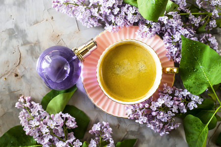 A beautiful still-life of lilac, a cup of coffee and a female perfume bottle. Spring mood concept. Top view, flat layの写真素材