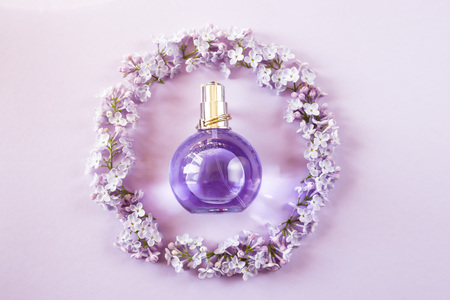 Violet bottle of women's perfume next to the flowers of lilac. Spring gentle fragrance for women. Top view, flat layの写真素材