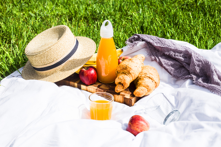 Summer picnic in the nature with croissants, juice and fruit on a white veil among the green grass. Leisure in natureの写真素材