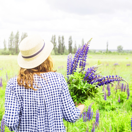 Caucasian girl in a blue dress with a hat is holding a bouquet of blue wildflowers of lupines in her hands. Recreation in the spring on a nature outside the city conceptの写真素材