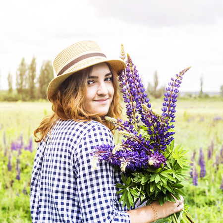 Caucasian girl is standing in a field with lupines and holding a bouquet of blue field flowers. Spring and summer outside the city conceptの写真素材