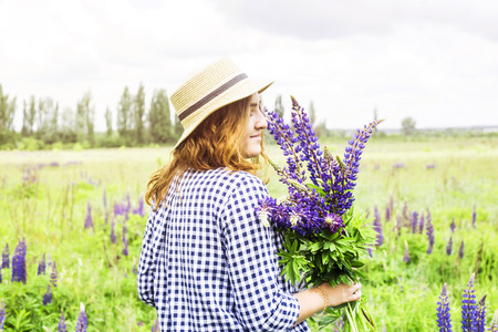 Caucasian girl in a blue dress with a hat is holding a bouquet of blue wildflowers of lupines in her hands. Recreation in the spring on a nature outside the city conceptの写真素材