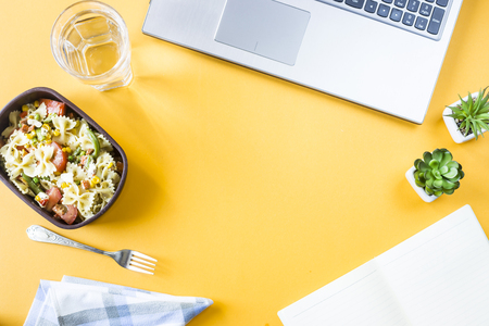 Vegetable salad with macaroni bowls with cheese in a container for lunch at the office workplace near the laptop. Top view, flat lay. Copyspaceの写真素材