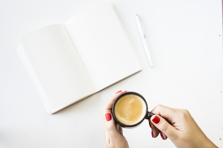 An open notebook with white clean sheets next to a white pen and a cup of coffee in female hands. Minimalism and creativity conceptの写真素材