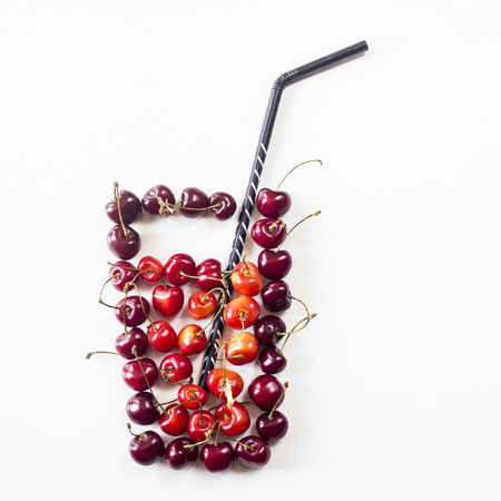 Yellow and dark red cherries on white lined with a glass with juice and a straw. Summer natural drink conceptの写真素材