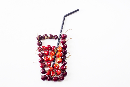 Yellow and dark red cherries on white lined with a glass with juice and a straw. Summer natural drink conceptの写真素材