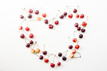Yellow and dark red cherries on white are lined in the shape of heart. Summer and love concept. Top view, flat layの写真素材