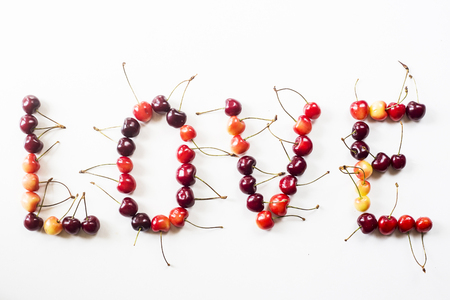 Yellow and dark red cherries on white are lined with the word love. Summer fruits and berries concept. Top view, flat layの写真素材
