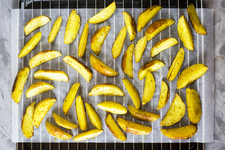 Baked potatoes on a baking sheet with pieces of spices and rosemary. Background. Top view, flat layの写真素材